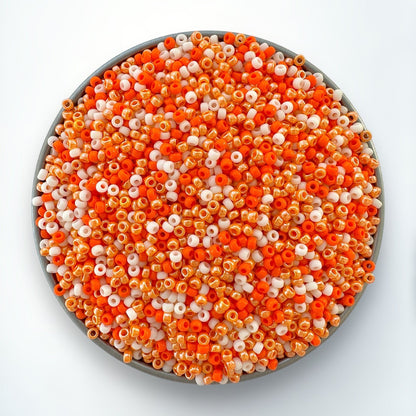 A mix of orange and cream 11/0 Miyuki seed beads by The Bead Mix in a silver container with a white background