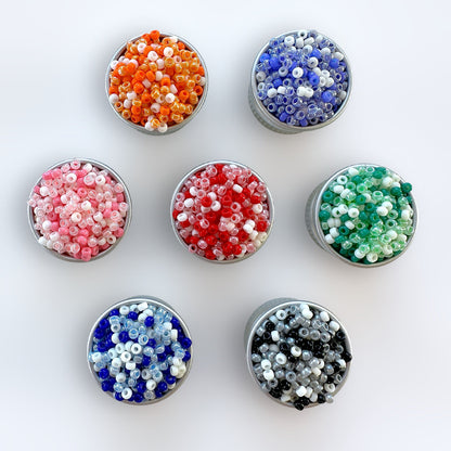 seven silver containers filled with Miyuki 11/0 seed beads in different colors, including pink, orange, green, red, blue, black and periwinkle on a white background