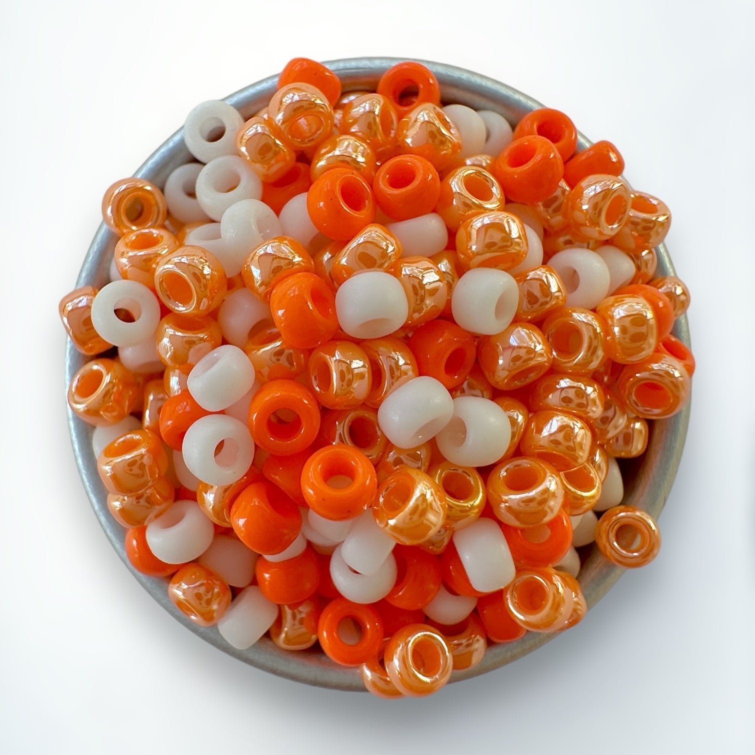 A mix of orange and cream 11/0 Miyuki seed beads by The Bead Mix in a silver container with a white background
