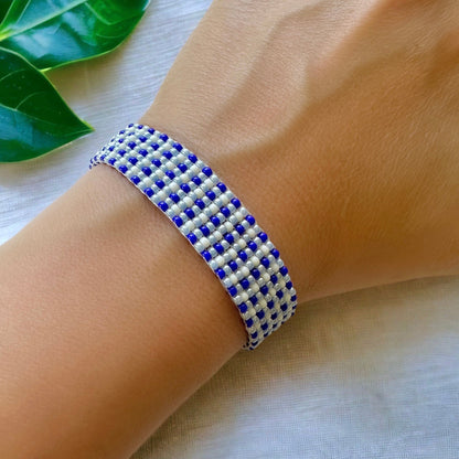 Beaded loom bracelet made with blue and cream 11/0 miyuki seed beads in a gingham pattern on a woman's wrist with a white cloth backdrop